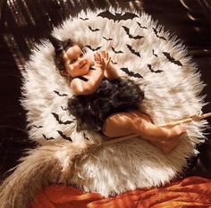 a baby laying on top of a white and black fur covered chair with bats around it