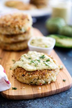 two crab cakes on a wooden cutting board with sauces and cucumbers in the background