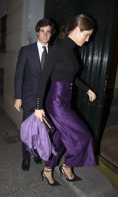 a man and woman are walking down the street with one holding a purple handbag