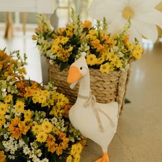 a duck statue sitting next to flowers in baskets on the floor with yellow and white flowers