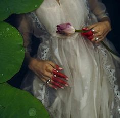 a woman in a white dress holding a pink flower next to a green lily pad