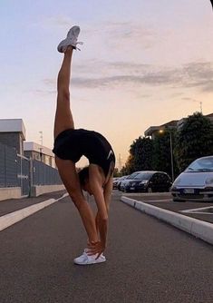 a woman doing a handstand in the middle of an empty parking lot at sunset