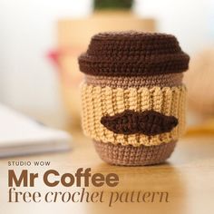 a crocheted coffee cup with a mustache on the top and bottom, sitting on a table