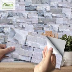 two hands are holding papers near a wall made out of stone blocks and paper with scissors on it