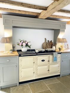 an old fashioned kitchen with grey cabinets and white walls, has flowers in a vase on the stove