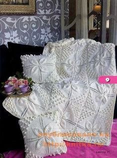 a white crocheted blanket sitting on top of a bed next to a vase with flowers