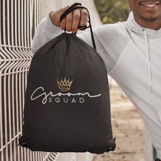 a man holding a black bag with the word squad on it and a crown drawn on it