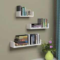 three white shelves with books on them next to a vase filled with flowers and other items