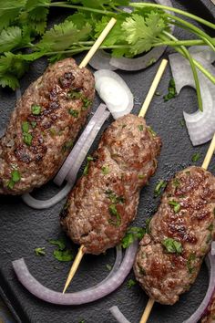 meat skewers with onions and cilantro on a black plate, ready to be served