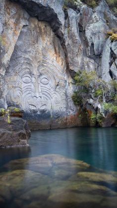 a rock face carved into the side of a cliff next to a body of water