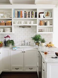 a kitchen with white cabinets and shelves filled with books, plants and other things on the counter