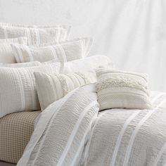 a bed with white linens and pillows on top of it, in front of a wall