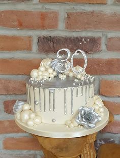 a wedding cake with white frosting and silver decorations on top, sitting in front of a brick wall