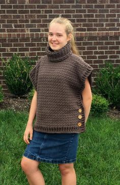 a woman standing in the grass wearing a brown knitted sweater with buttons on it