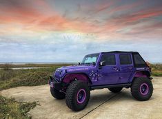 a purple jeep parked on top of a dirt road next to a body of water