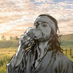 a drawing of jesus drinking from a glass in front of a grassy field at sunset