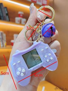 a person holding a gameboy keychain in their left hand with measurements on it