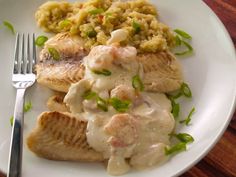 a white plate topped with fish covered in gravy next to rice and a fork