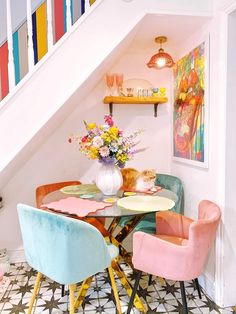 a dining room table with colorful chairs under the stairs