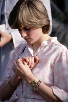 a young woman wearing a pink shirt and bracelets looking down at her watch while standing in front of other people