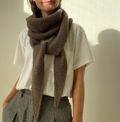 a woman wearing a brown scarf standing in front of a white wall with her hands on her hips