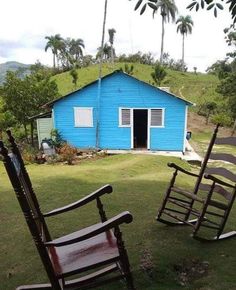 two wooden rocking chairs sitting in front of a blue house on the side of a hill