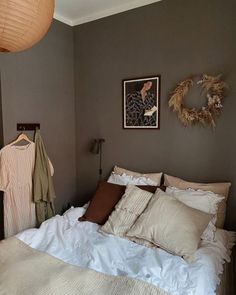 a bed with white sheets and pillows next to a brown wall hanging on the wall