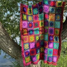 a multicolored crocheted blanket hanging from a tree