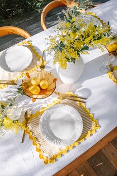 the table is set with yellow and white plates, vases, and napkins