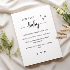 a baby announcement with clothes pins and flowers next to it on a white sheet that says, don't say baby