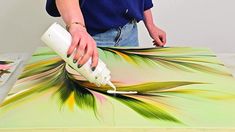 a woman is painting an art piece with white paint and green leaves on the table