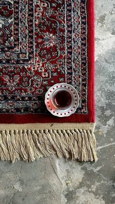 a cup of coffee sitting on top of a red rug next to a black and white vase