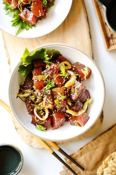 two white plates filled with food on top of a wooden cutting board next to chopsticks