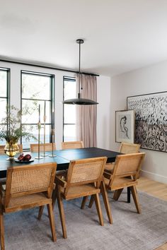 a dining room table with chairs and artwork on the wall in front of large windows