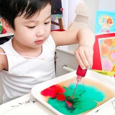 a little boy is painting with red and green paints on a white tray in front of him