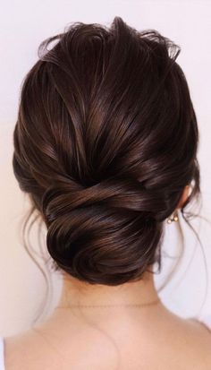 a woman with dark brown hair in a low bun updo, looking back at the camera