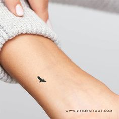 a woman's arm with a small black bird tattoo on the left side of her arm