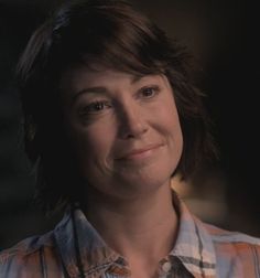 a close up of a person wearing a plaid shirt and looking at the camera with a smile on her face