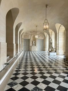 an ornate hallway with black and white checkered flooring, chandeliers and statues