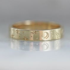 Why I Love It: A band that is perfect for any time of day or night in this wider version of our best selling star engraved bands. Swift and careful hand movements create this motif of crescent moons, stars, planets and sun rays that pure celestial ring vibes. Engraved texture with precise detail and extraordinary design in your choice of golds. All hand engraved locally in San Francisco, CA. The Details: 14k Yellow Gold, 14k White Gold, 14k Rose Gold, 18k Peach Gold Band Width is Approx. 3.50 mm Engraved Gold Band, Cosmic Wedding, Wedding Ring Engraved, Hand Engraved Rings, خواتم خطوبة, Hand Movements, Extraordinary Design, Wedding Band Engraving, Celestial Ring