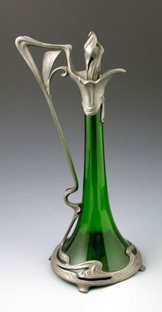 a green glass vase sitting on top of a white table next to a silver object