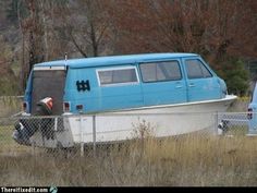 an old blue van is parked behind a fence in a field with tall grass and trees