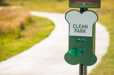 a sign that says clean park on it next to a path with grass and trees in the background