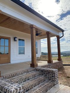 a porch with brick steps leading up to the front door and covered patio area, under a partly cloudy blue sky