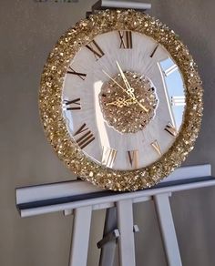 a clock that is sitting on top of a white stand with gold numbers and roman numerals