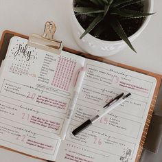 an open planner and pen sitting on top of a desk next to a potted plant