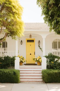 a yellow door sits on the front steps of a white house with potted plants