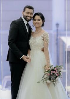 a bride and groom standing next to each other in front of a glass wall holding hands