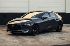 a black mazda car parked in front of a garage with two doors and no windows