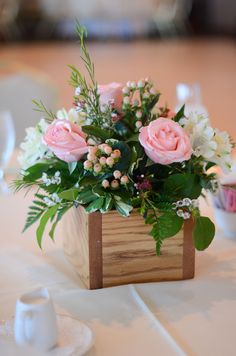 pink roses and white flowers in a wooden box on a table with teacups